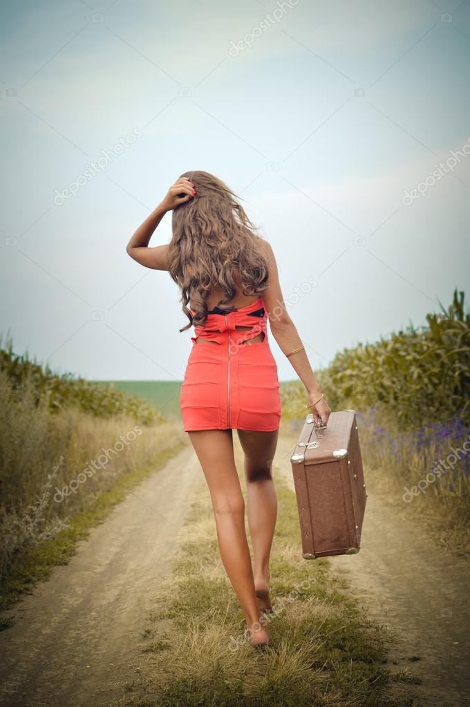Image of beautiful young woman holding suitcase in hand and walking on sunny day outdoors landscape