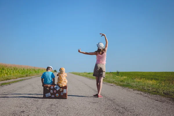 Giovane donna che balla vicino a due bambini con valigia su strada — Foto Stock