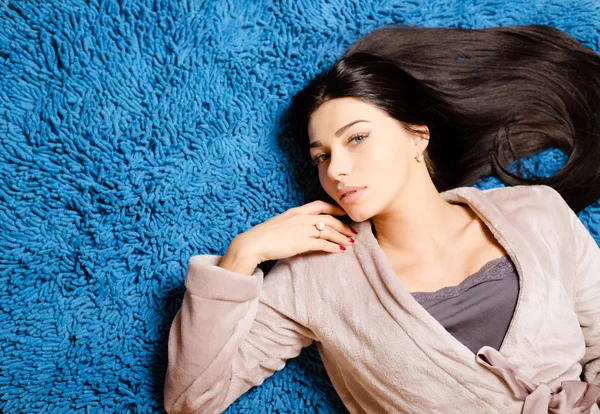 Young girl in silky robe lying on blue fluffy carpet — Stock Fotó