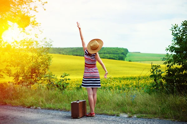 Girl with old suitcase standing on roadside in sun flare — Stockfoto