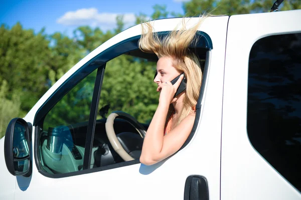 Chica joven con el pelo soplado en el coche hablando por teléfono — Foto de Stock