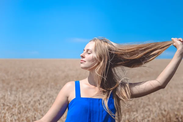 Девушка закрывает глаза на голубое небо и пшеничное поле фона — стоковое фото