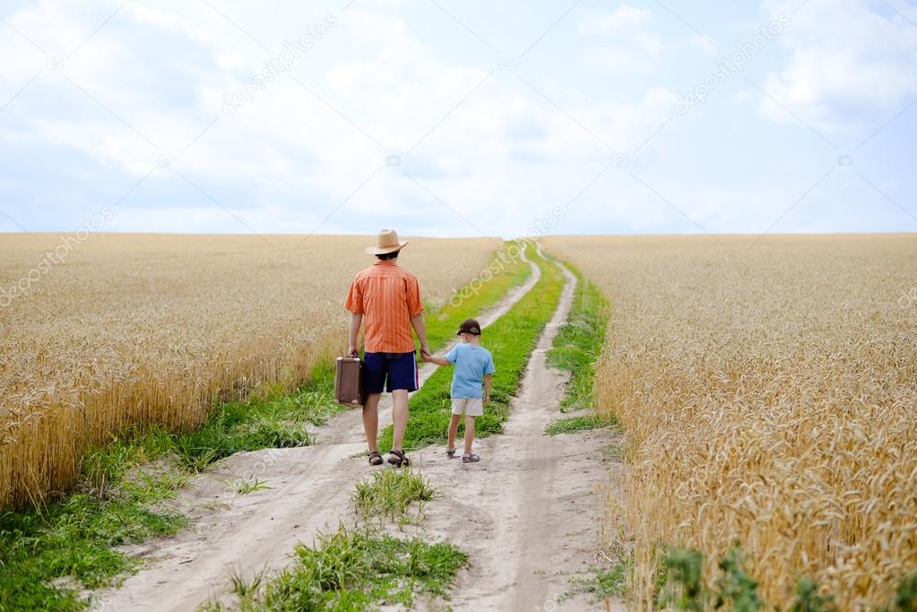 Man with suitcase and boy walking away in wheat field