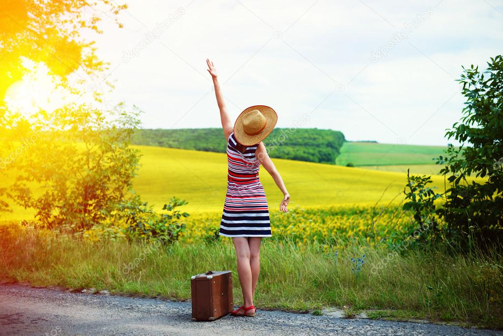 Girl with old suitcase standing on roadside in sun flare