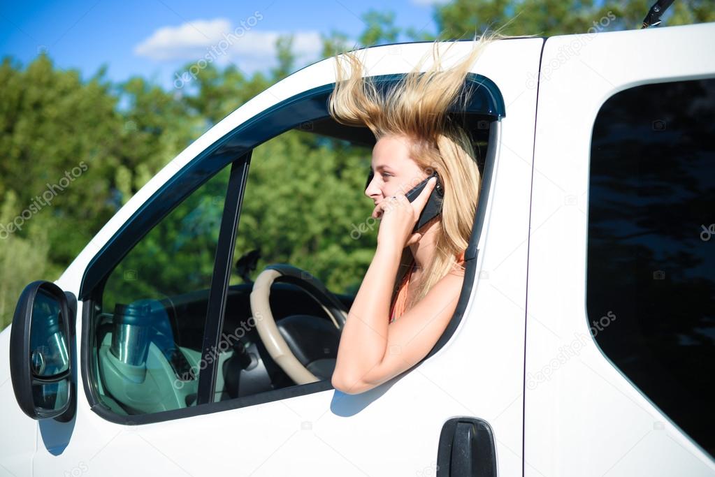 Young girl with blowed hair in car speaking by phone