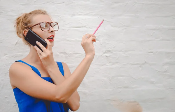 Girl wearing big glasses speaking phone and drawing in air — Stock Photo, Image