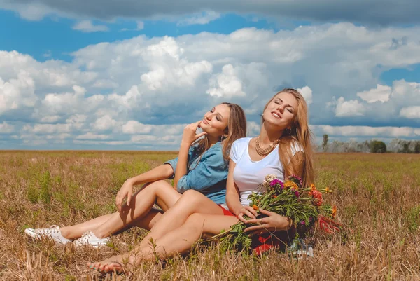 Two girls sitting on meadow with wildflowers and enjoying sunlight — Stock Photo, Image