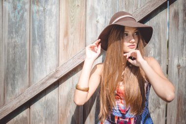Young beautiful woman in hat and tiger print top beside fence
