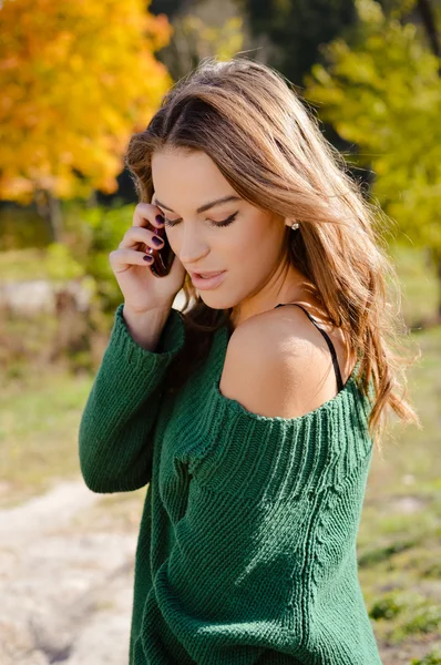 Beautiful woman in green sweater speaking phone on autumn background — 스톡 사진