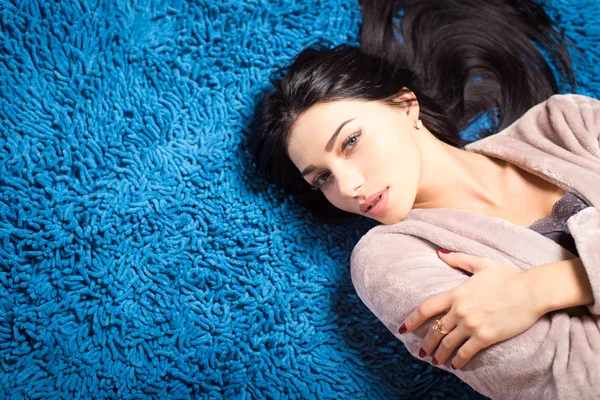 Mujer bonita en bata beige acostada en la alfombra de espagueti azul — Foto de Stock