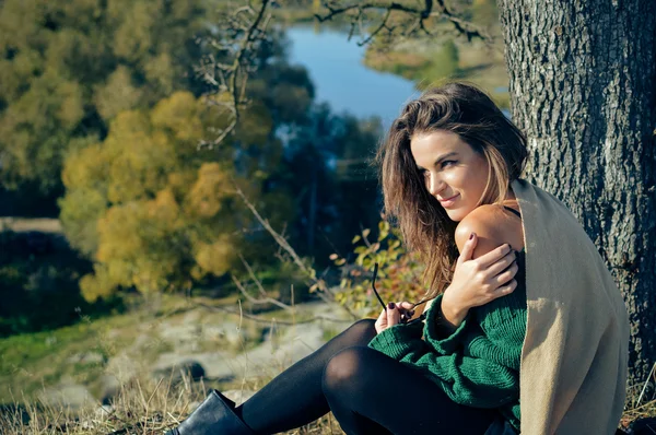 Young girl wearing green sweater sitting under tree in autumn — Stock fotografie