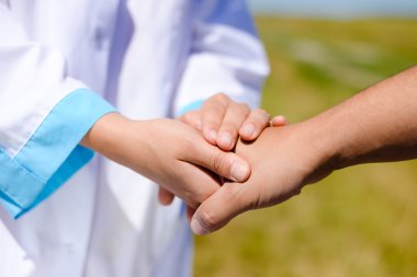 Close up picture of handshake between doctor and patient on sunny day over green outdoors and blue sky background
