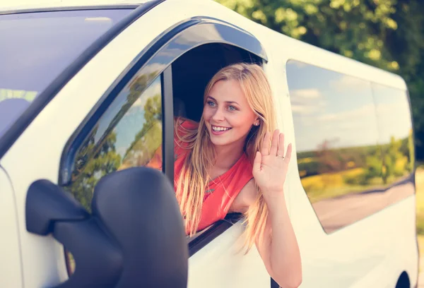 Imagen de la hermosa chica rubia sonriendo y saludando a alguien desde la ventana del coche . — Foto de Stock