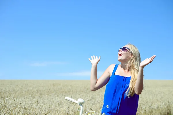 Picture of young beautiful blonde woman in sunglasses looking up sitting on bicycle in the middle of wheat field — Stok fotoğraf