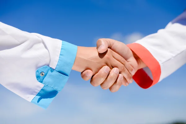 Closeup picture of handshake between doctors over blue sky sunny outdoors background — Stock Photo, Image