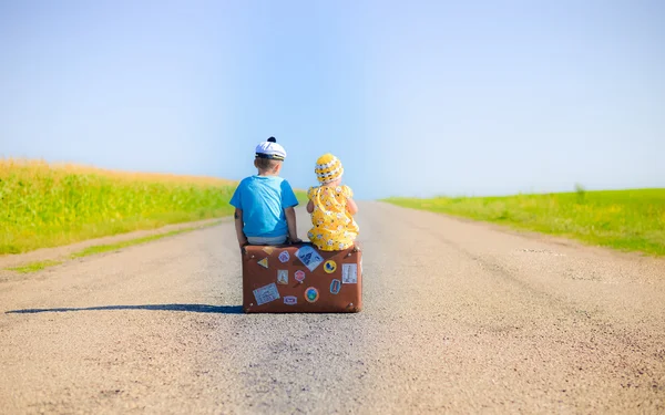 Children on the suitcase over countryside rural road on sunny blue sky outdoors background, back view photography