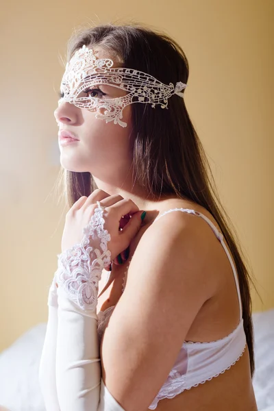 Sexy beautiful girl in white lingerie and lace mask, gloves sitting on bed. — Stockfoto