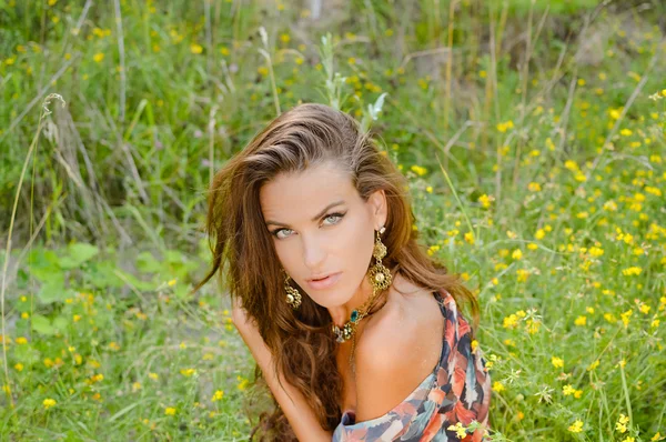 Sexy girl in ethnic earrings and necklace sitting on grass — Stock Fotó