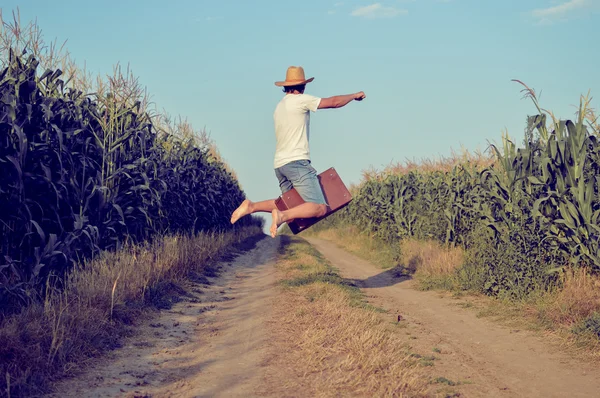 Male flying or jumping with suitcase on country road in field — Stock Photo, Image