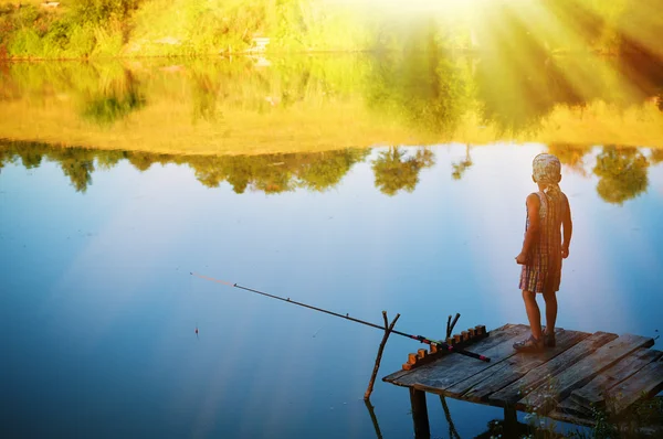 Little boy standing alone on riverside pier fishing with rod — Stockfoto