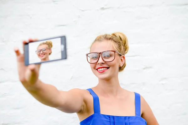 Щаслива дівчина робить селфі зі смартфоном на білому тлі стіни — стокове фото