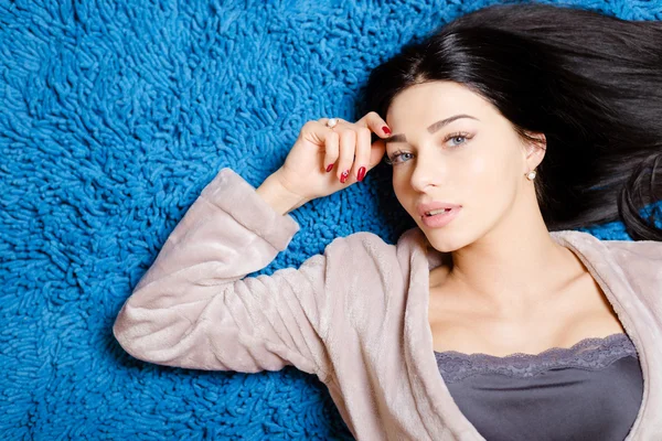 Красива дівчина в затишному халаті, що лежить на синьому пухнастому килимі — стокове фото