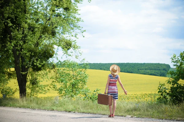 Ragazza in cappello di paglia con valigia retrò vicino al prato estivo — Foto Stock