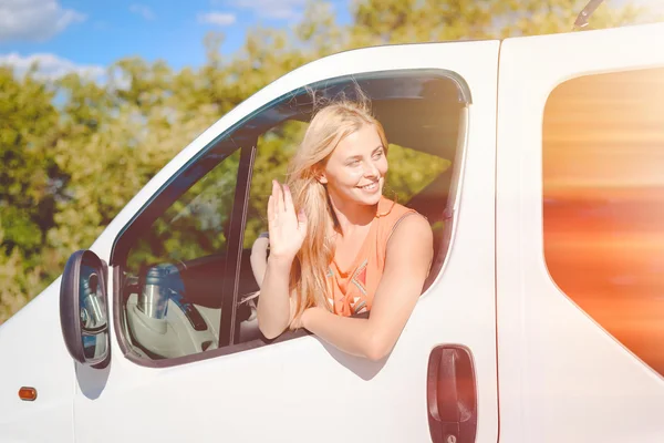 Chica rubia feliz sonriendo y saludando a alguien desde la ventana del coche — Foto de Stock