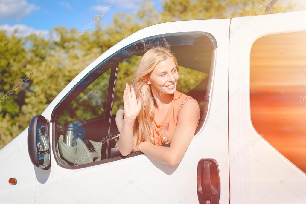Blond girl happy smiling and greeting someone from car window