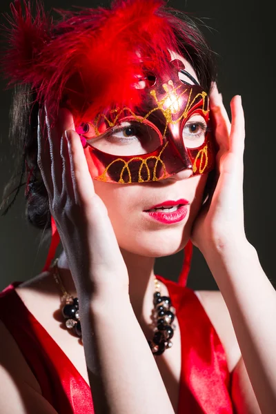Mujer bonita en vestido rojo sosteniendo la máscara y mirando a un lado — Foto de Stock