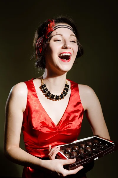 Молодая девушка в винтажном платье смеется и держит шоколадные конфеты — стоковое фото