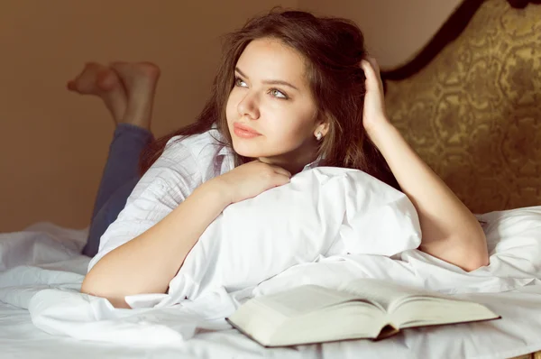 Мрійлива красива дівчина-підліток лежить на ліжку з відкритою книгою, що вивчає — стокове фото