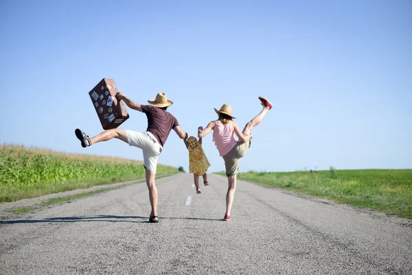 Parents and baby with suitcase jumping and dancing on road — Zdjęcie stockowe