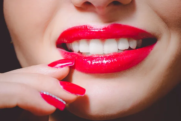 Closeup of pearly smile with red lips and red nails