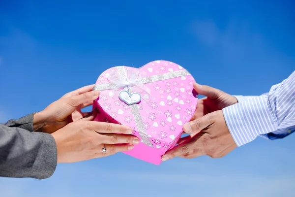 Mans hands giving pink heart shaped box to womans hands — Zdjęcie stockowe