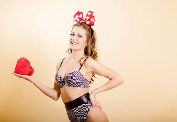 Smiling pinup girl holding red heart over cream background — Stockfoto