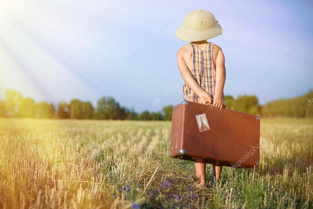 Kid with old suitcase walking away on sunny flare background