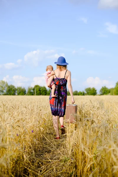 Young mother travelling with her child on hand on the wheat field — Stockfoto