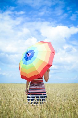 Romantic lady holding umbrella and standing in golden wheat field over blue sky