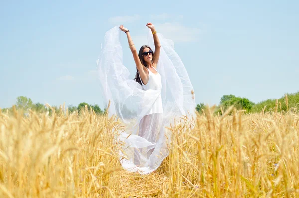 Brunette girl wearing white dress standing in golden wheat field — ストック写真