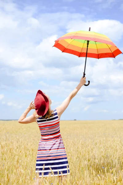 Girl wearing red hat rising umbrella and standing in wheat field — Stock Photo, Image