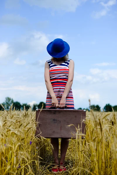 Mulher elegante usando chapéu com valize caminhando através do campo de trigo . — Fotografia de Stock