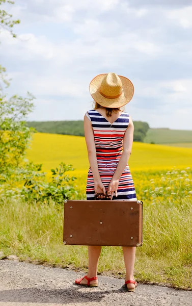 Picture of female holding old suitcase standing on roadside near summer field — Zdjęcie stockowe