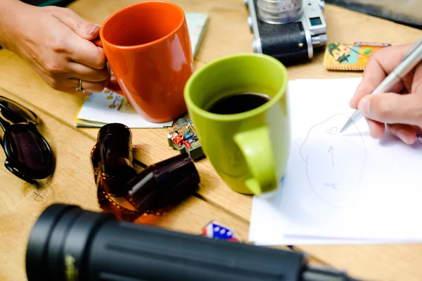 Hand holding coffee mug and sketch writing hand with camera — Stockfoto