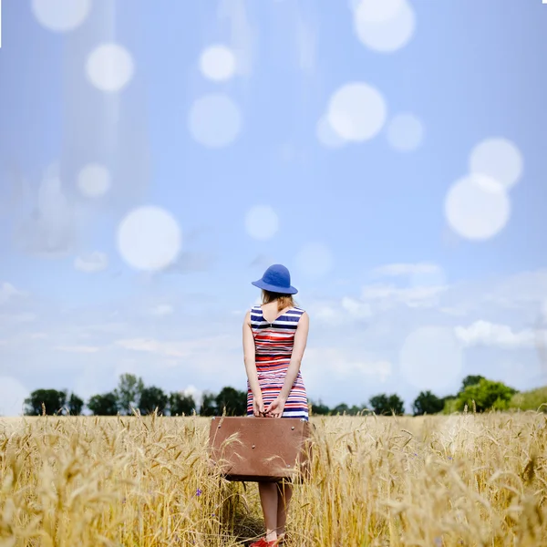 Girl standing with suitcase in wheat field with lens flare — Stock Photo, Image