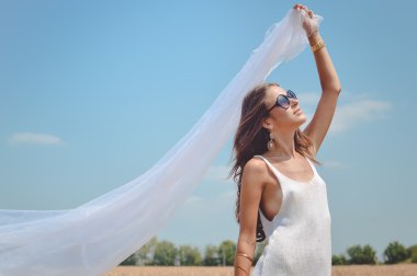Picture of joyful romantic beautiful female holding light fabric and enjoying outdoors looking up on wheat field and blue sky background