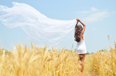 Image of joyful romantic beautiful young lady holding light fabric on open field and enjoying outdoors looking up over blue sky