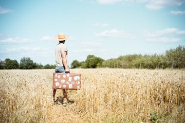 Man in straw hat holding old suitcase in wheat field