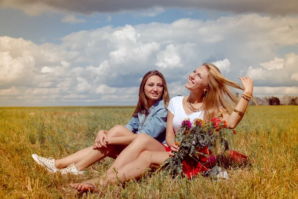 Two beautiful young women sitting on summer meadow with wildflowers — Stock Photo, Image