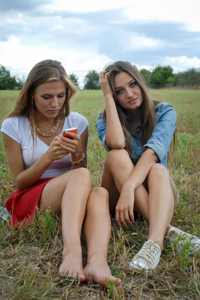 Two beautiful young ladies sitting together on summer green meadow — Stock Photo, Image